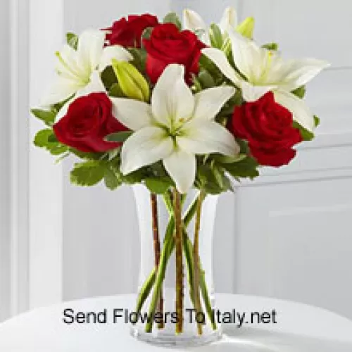Des roses rouges et des lys blancs avec quelques remplissages saisonniers dans un vase en verre